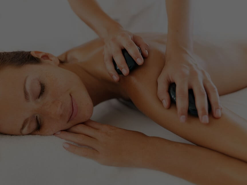 Person lying down with eyes closed, receiving a hot stone massage treatment with two smooth stones.